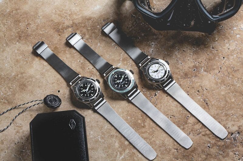 Serica 5303 Black, White & midnight blue watches laid down next to tag and case 